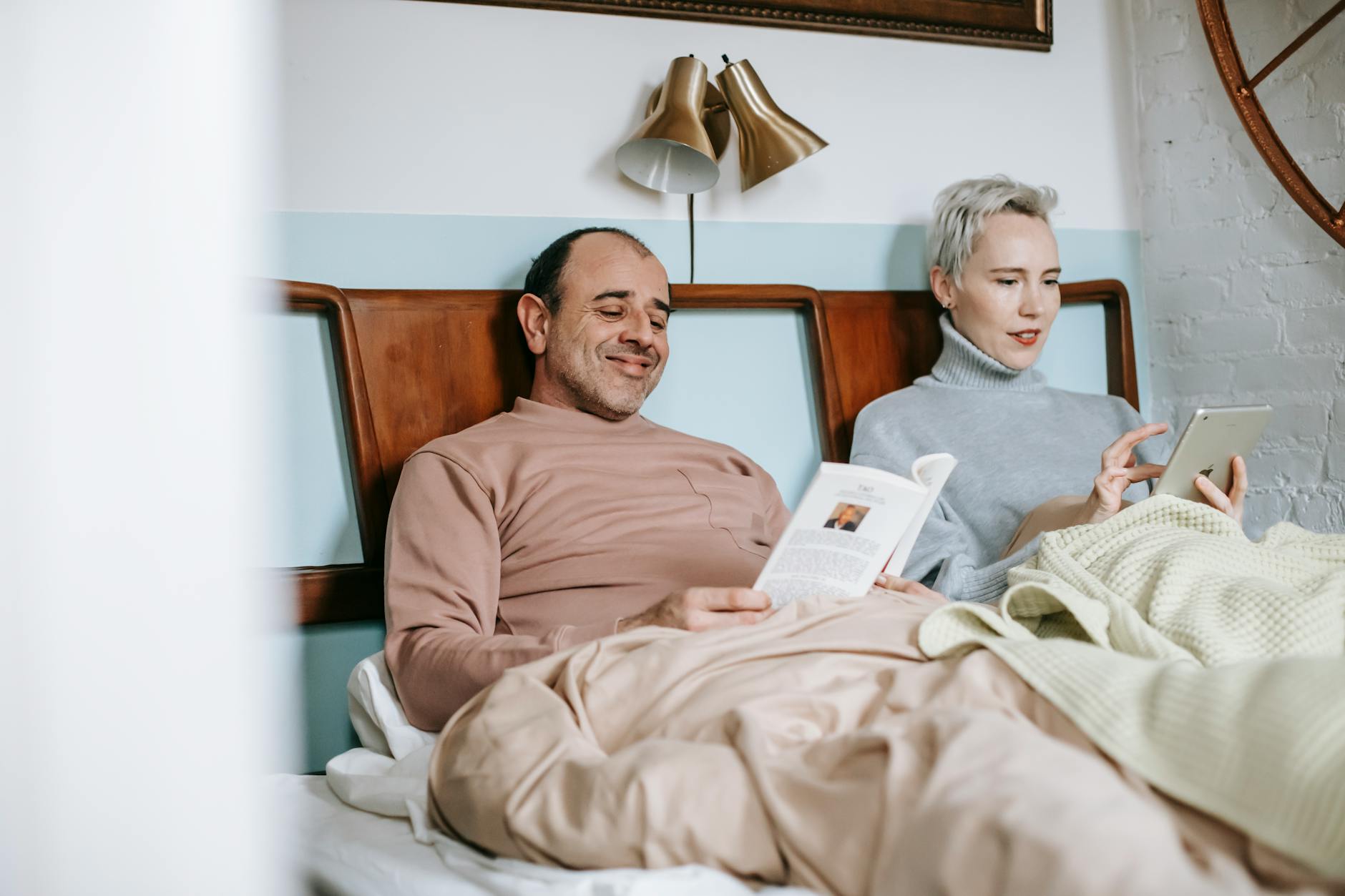 adult diverse married couple reading book and using table in bed