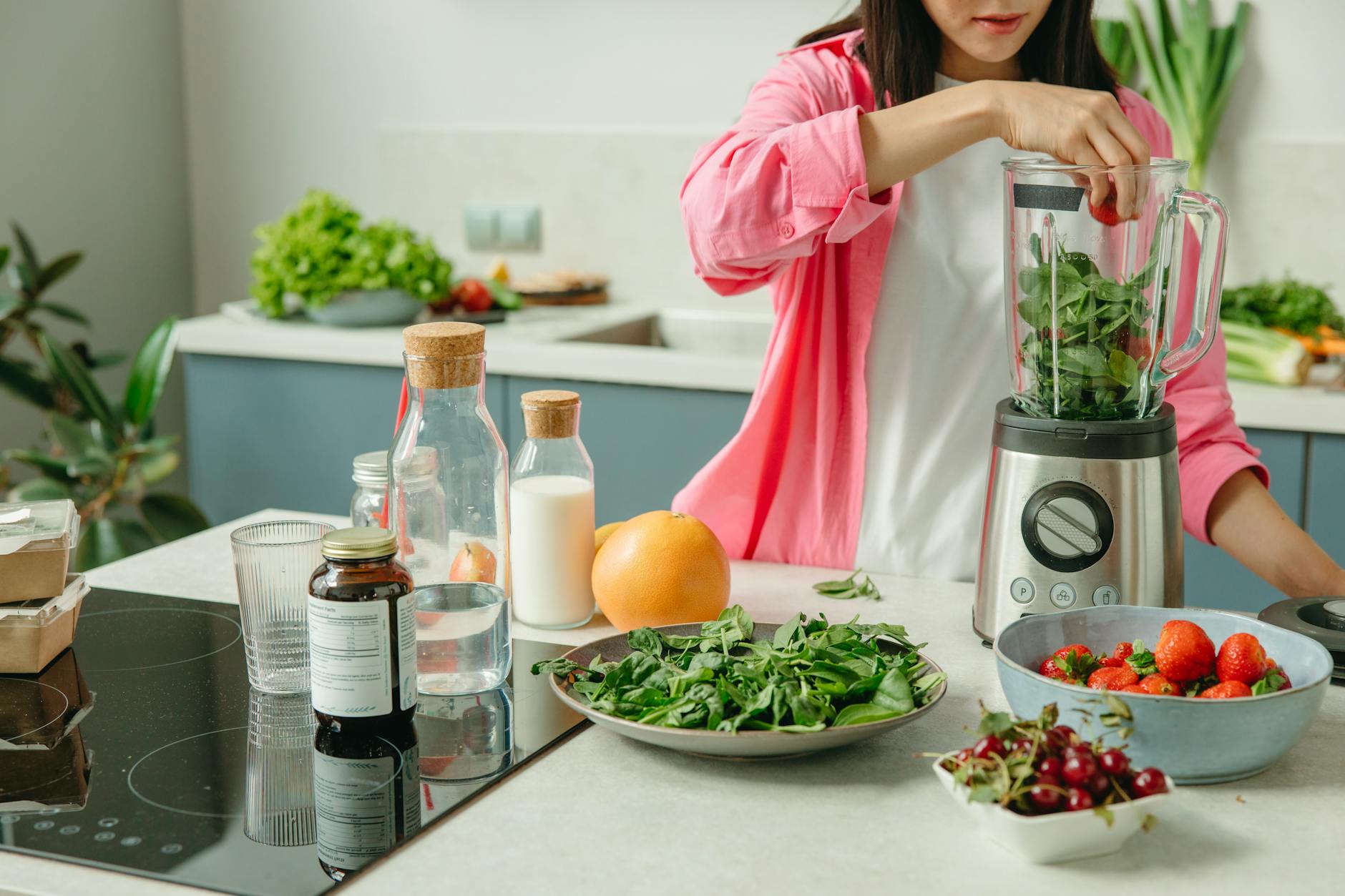 a woman putting the green leaves and strawberries in the blender